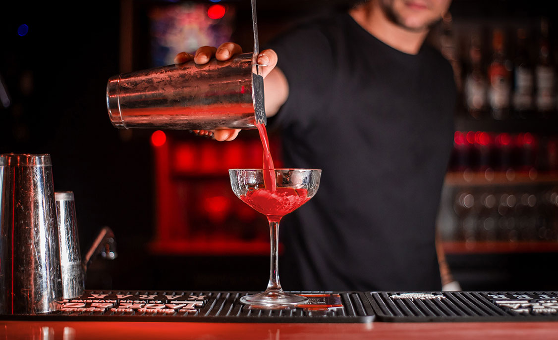 Bartender pouring drink into martini glass